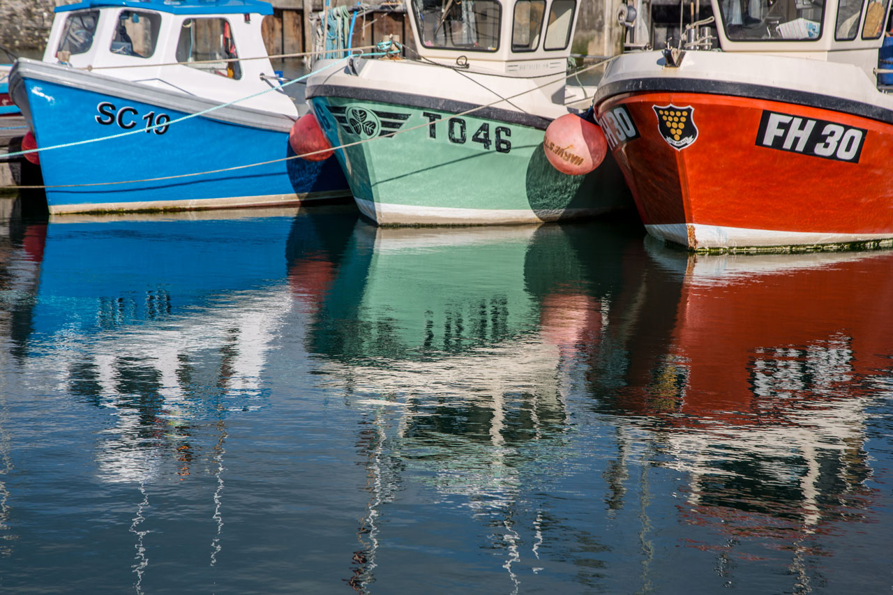 three bright fishing boats up close in Padstow Harbour.